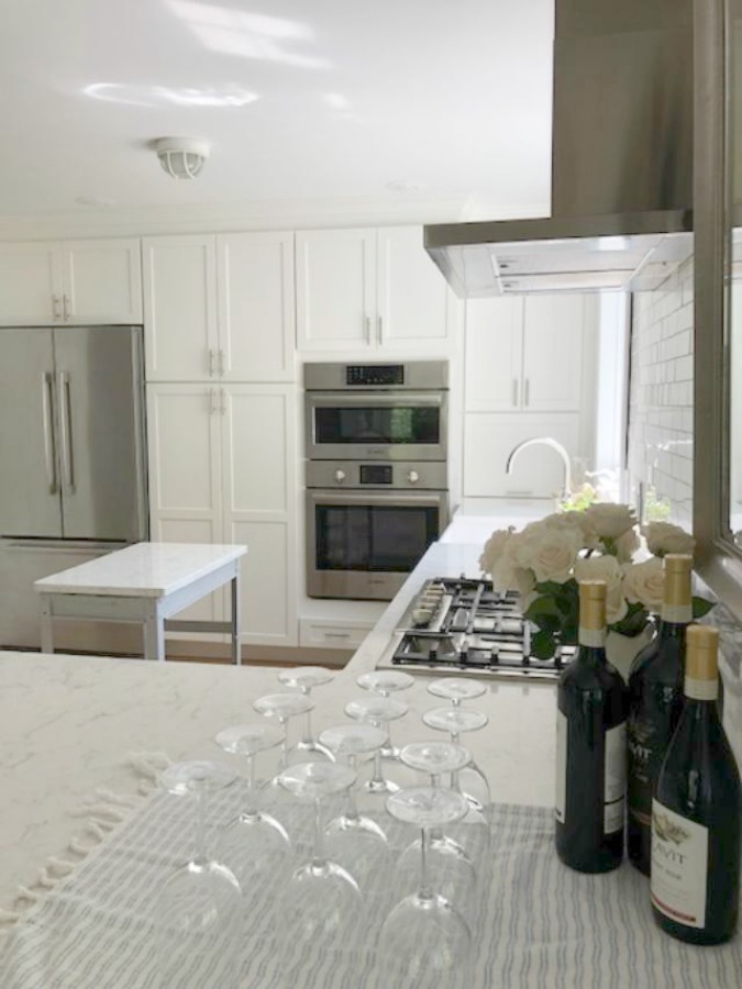 Serene tranquil white kitchen with farm sink, marble subway tile, Viatera Minuet quartz counters, white Shaker cabinets, and white oak flooring. Design and photo: Hello Lovely Studio. #kitchendesign #whitekitchen #minuet #whitequartz #benjaminmoorewhite