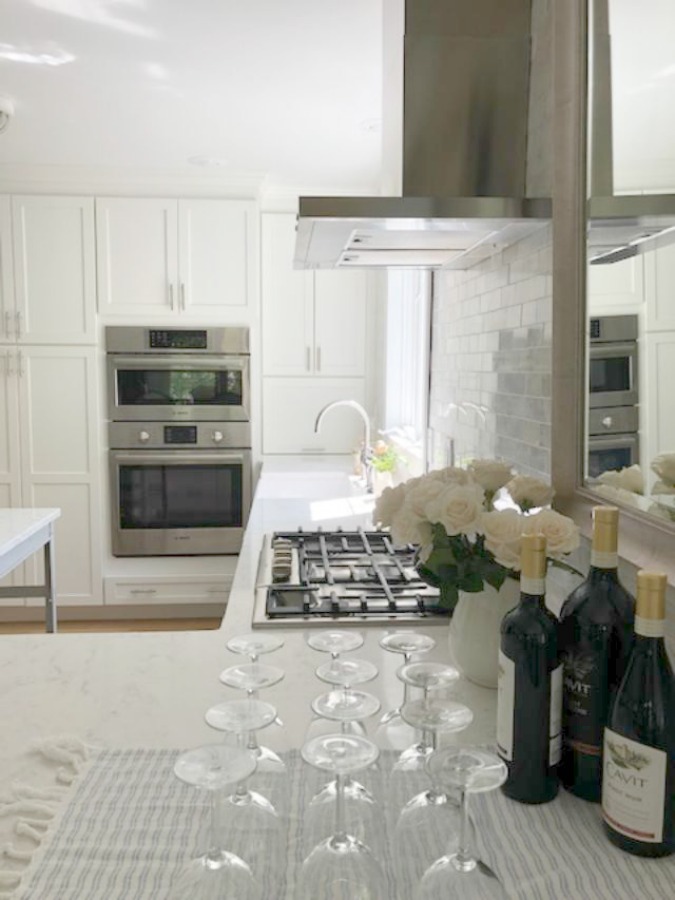 Serene tranquil white kitchen with farm sink, marble subway tile, Viatera Minuet quartz counters, white Shaker cabinets, and white oak flooring. Design and photo: Hello Lovely Studio. #kitchendesign #whitekitchen #minuet #whitequartz #benjaminmoorewhite