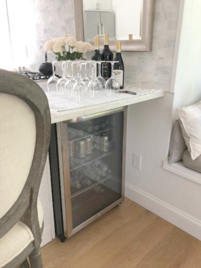 Serene tranquil white kitchen with farm sink, marble subway tile, Viatera Minuet quartz counters, white Shaker cabinets, and white oak flooring. Design and photo: Hello Lovely Studio. #kitchendesign #whitekitchen #minuet #whitequartz #benjaminmoorewhite