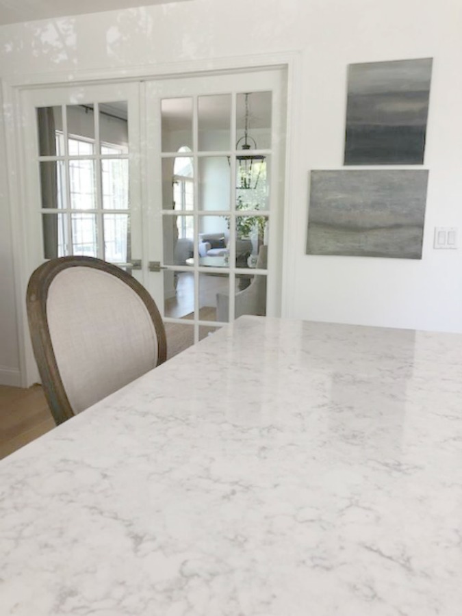 Serene tranquil white kitchen with farm sink, marble subway tile, Viatera Minuet quartz counters, white Shaker cabinets, and white oak flooring. Design and photo: Hello Lovely Studio. #kitchendesign #whitekitchen #minuet #whitequartz #benjaminmoorewhite