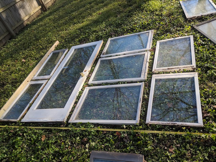 Vintage windows arranged on ground in preparation for a DIY greenhouse. Come explore She Shed Chic, Potting Shed & Backyard Inspiration.