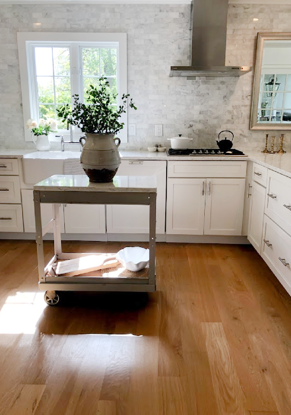 Hello Lovely's white European country modern French kitchen with Minuet Viatera quartz counters, farm sink, industrial cart, and marble subway backsplash.