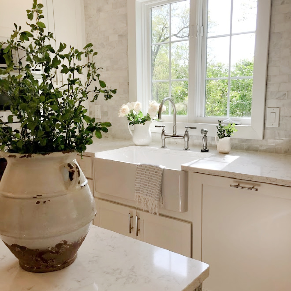 Hello Lovely's white European country modern French kitchen with Minuet Viatera quartz counters, farm sink, industrial cart, and marble subway backsplash.