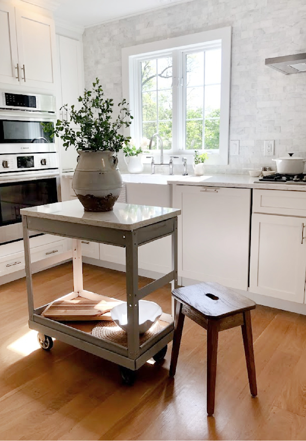 Hello Lovely's white European country modern French kitchen with Minuet Viatera quartz counters, farm sink, industrial cart, and marble subway backsplash.