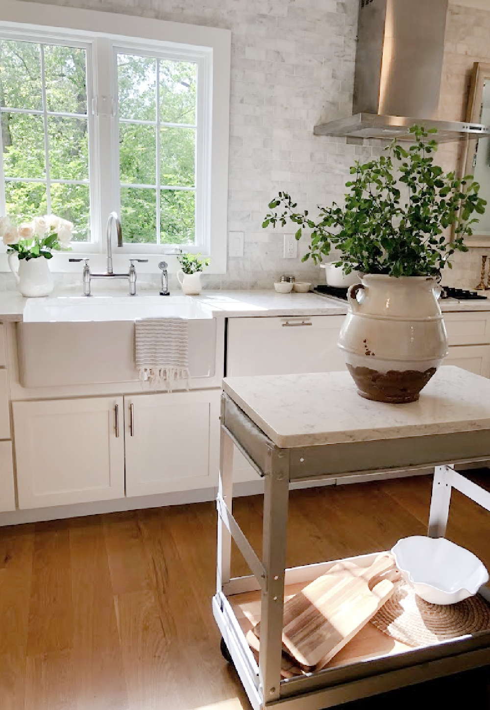 Hello Lovely's white European country modern French kitchen with Minuet Viatera quartz counters, farm sink, industrial cart, and marble subway backsplash.