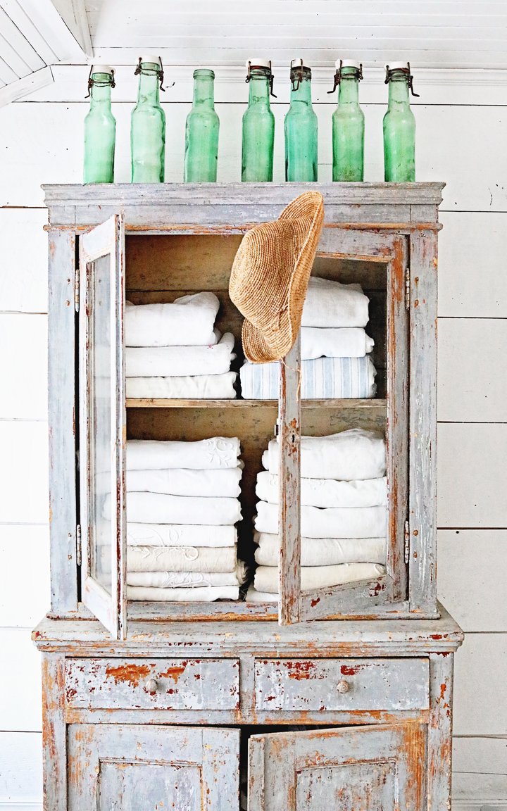 Weathered blue grey vintage wood cabinet with white towels inside. French canning jars decorate the top, and shiplap adorns the wall behind it. Dreamy Whites Atelier. #frenchfarmhouse #bluegry #shabbychic