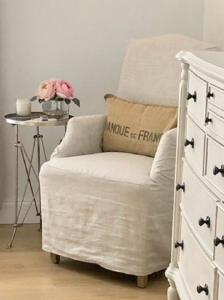 Benjamin Moore White on walls of Hello Lovely Studio's European country bedroom with Belgian linen slipcovered chair. #benjaminmoore #whitepaints #interiordesign #paintcolors