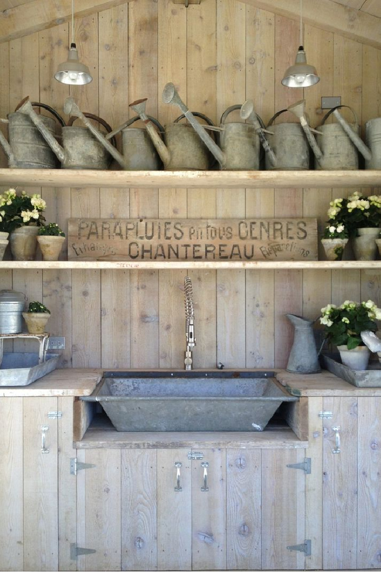 Vintage galvanized watering can collection and French antique sign in garden shed at Patina Farm, a European country French farmhouse inspired home by Brooke Giannetti and Steve Giannetti. #wateringcans #frenchfarmhouse #gardenshed #patinafarm