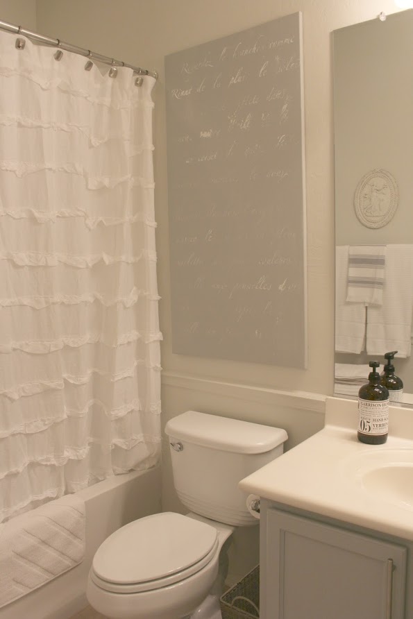 French script stenciled canvas in a serene bathroom by Hello Lovely Studio. Paint color on canvas is Behr Classic Silver and on walls is Valspar Salute. Click through for Perfect Light Gray Paint Colors You'll Love as Well as Interior Design Inspiration Photos. #bestgreypaint #paintcolors