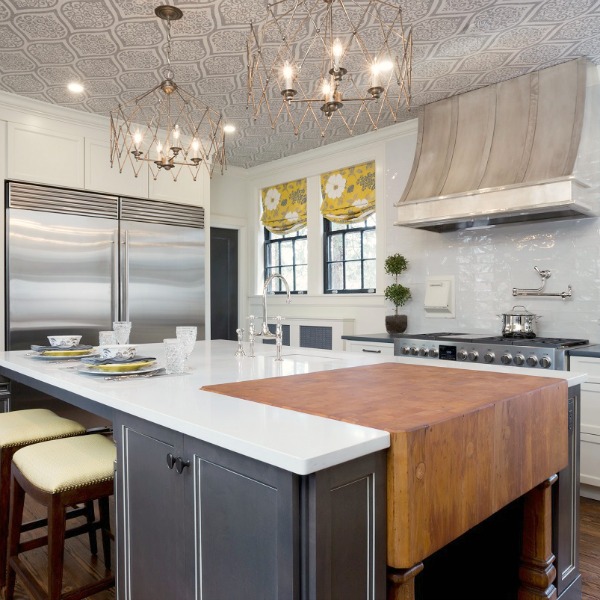 Beautiful renovated white classic kitchen in Julian Price Mansion with subway tile, farm sink, and yellow accents. Marsh Kitchens executed the lovely design which features black windows, warm wood floors, butcher block insert in huge island, and luxury range and hood.