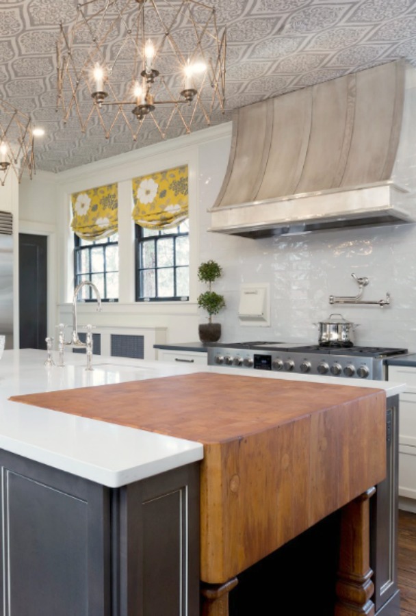 Beautiful renovated white classic kitchen in Julian Price Mansion with subway tile, farm sink, and yellow accents. Marsh Kitchens executed the lovely design which features black windows, warm wood floors, butcher block insert in huge island, and luxury range and hood.