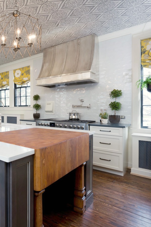 Beautiful renovated white classic kitchen in Julian Price Mansion with subway tile, farm sink, and yellow accents. Marsh Kitchens executed the lovely design which features black windows, warm wood floors, butcher block insert in huge island, and luxury range and hood.