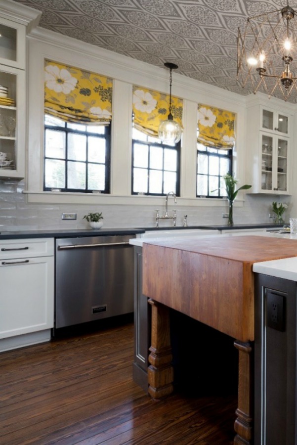 Beautiful design details in the renovated white classic Julian Price House kitchen with subway tile, farm sink, and yellow accents. Marsh Kitchen & Bath executed the lovely design which features black windows, warm wood floors, butcher block insert in huge island, and luxury range and hood.