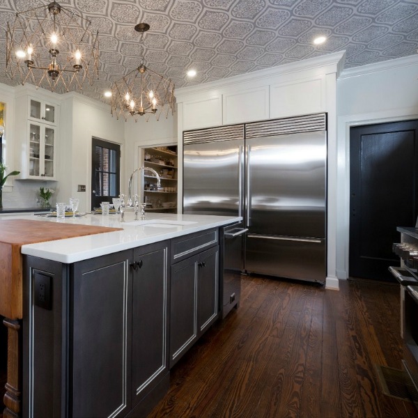 Beautiful design details in the renovated white classic Julian Price House kitchen with subway tile, farm sink, and yellow accents. Marsh Kitchen & Bath executed the lovely design which features black windows, warm wood floors, butcher block insert in huge island, and luxury range and hood.