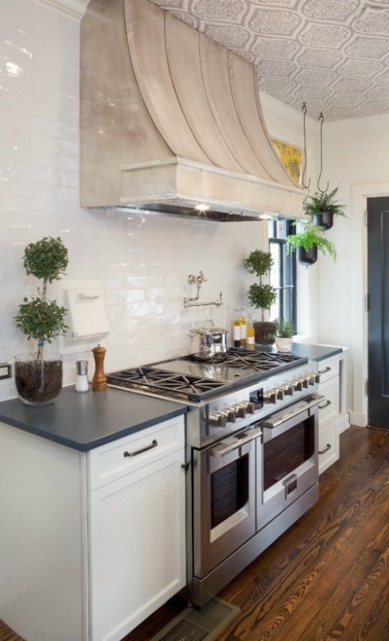Beautiful design details in the renovated white classic Julian Price House kitchen with subway tile, farm sink, and yellow accents. Marsh Kitchen & Bath executed the lovely design which features black windows, warm wood floors, butcher block insert in huge island, and luxury range and hood.