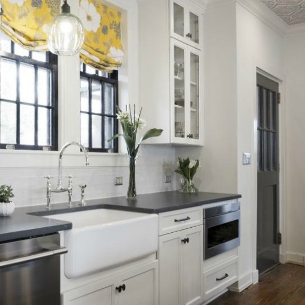 Beautiful design details in the renovated white classic Julian Price House kitchen with subway tile, farm sink, and yellow accents. Marsh Kitchen & Bath executed the lovely design which features black windows, warm wood floors, butcher block insert in huge island, and luxury range and hood.