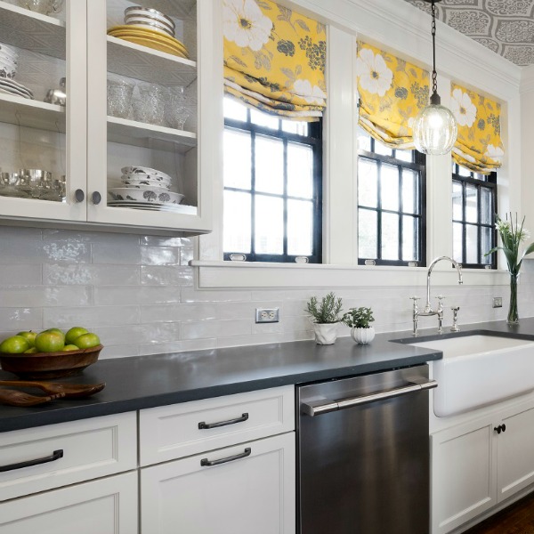 Beautiful design details in a renovated white classic kitchen with subway tile, farm sink, and yellow accents. Marsh Kitchen & Bath executed the lovely design which features black windows, warm wood floors, butcher block insert in huge island, and luxury range and hood.