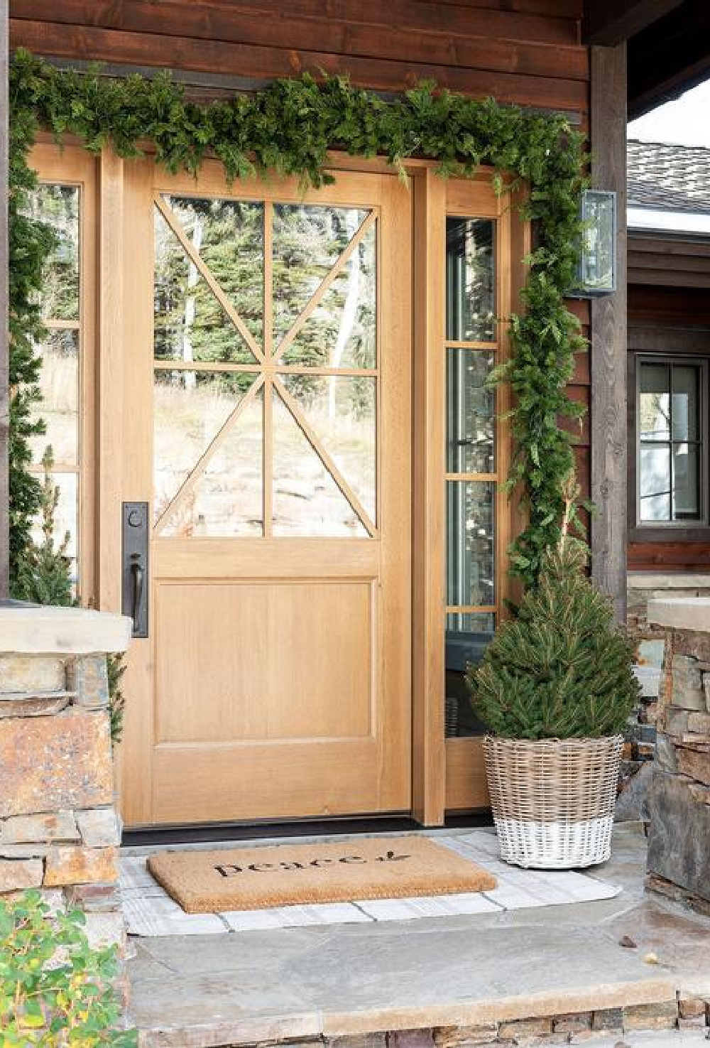 Gorgeous rustic wood front door, garland, peace door mat layered on plaid rug - McGee & Co.