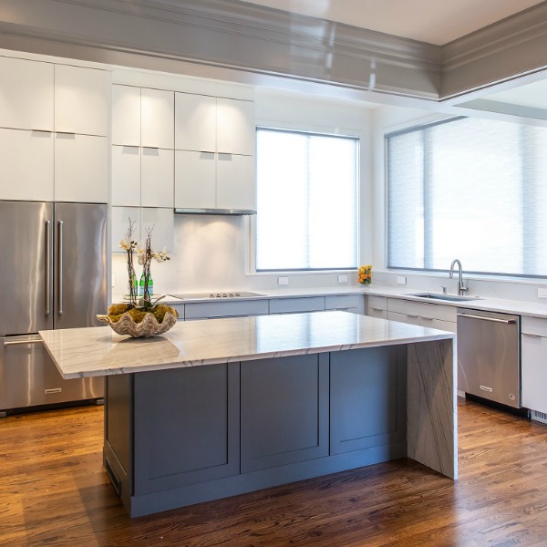 Beautiful kitchen design with white cabinets, waterfall countertop, and warm wood floors by Marsh Kitchens on Hello Lovely.