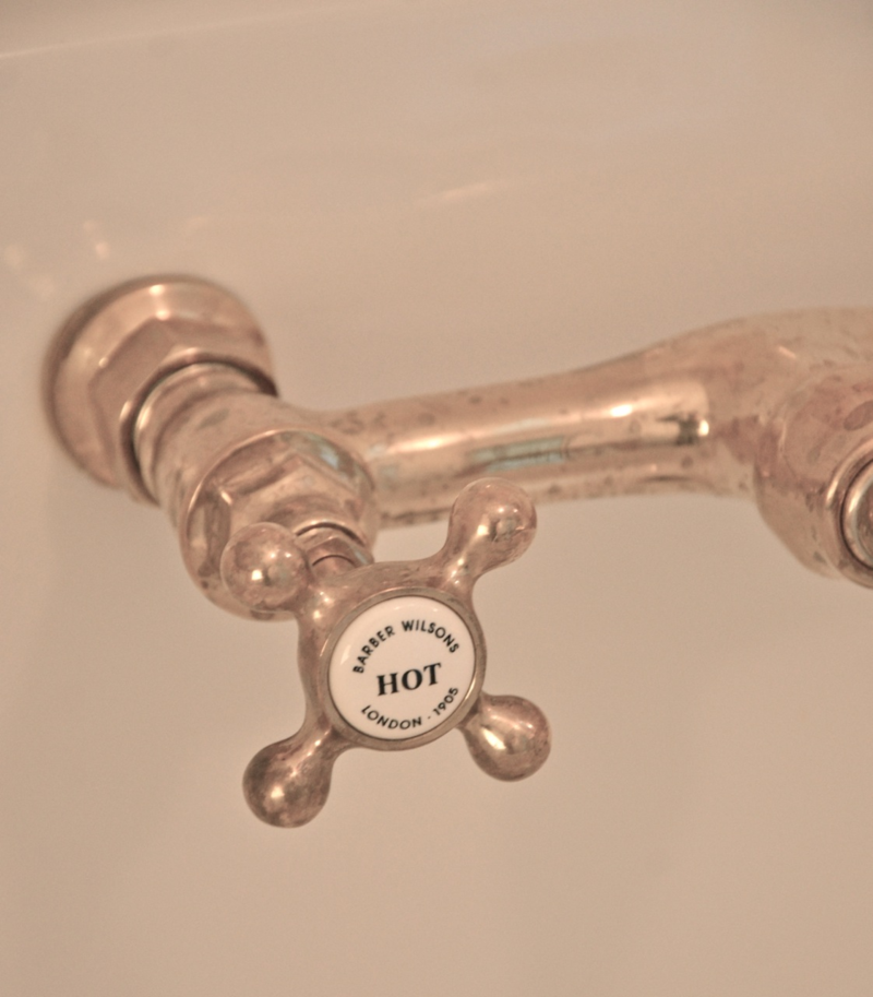 Unlaquered brass detail of Barber Wilsons wall mount bridge faucet in Patina Farm laundry room. Giannetti Home.