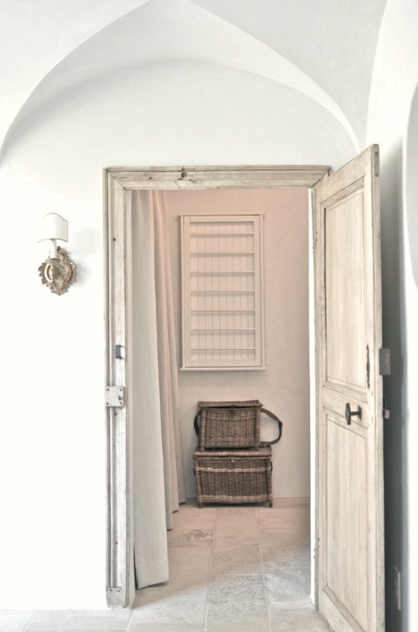 A vintage door opens to a lovely laundry room with rustic French farmhouse style and a wall mounted drying rack. Patina Farm by Giannetti Home.