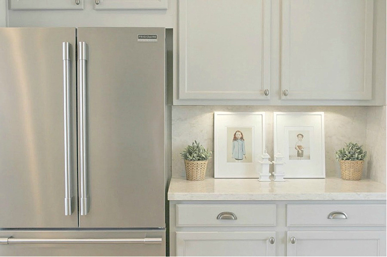 Serene kitchen makeover with Viatera white quartz (Soprano), painted cabinets (Behr Classic Silver), hardware (Top Knobs), and Kitchenaid Smudgeproof appliances - Hello Lovely Studio. #kitchenmakeover #beforeafter #diykitchenreno #kitchendesign #paintedcabinets #viateraquartz #soprano #homereno