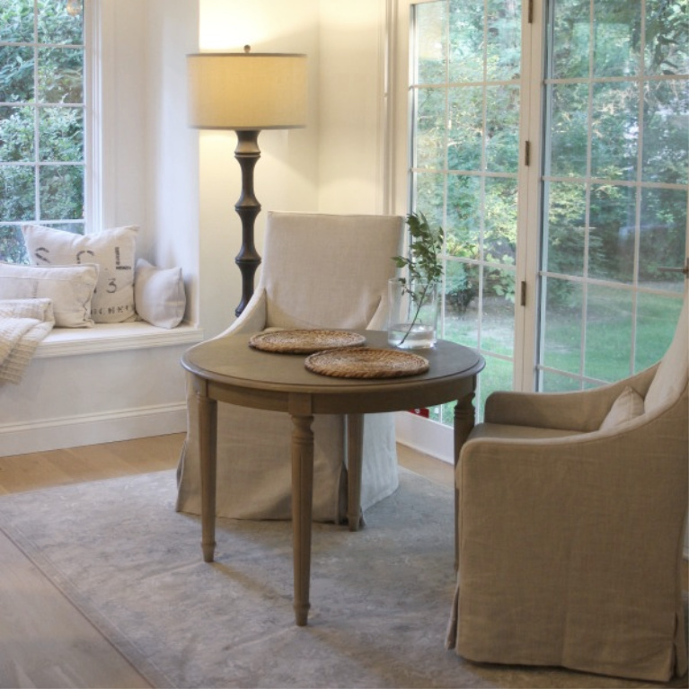 Window seat with European inspired pillows and Belgian linen slipcovered dining chairs in a breakfast area of a French country kitchen - Hello Lovely Studio. #frenchcountry #kitchendesign #breakfastroom #belgianlinen #windowseat #serenedecor