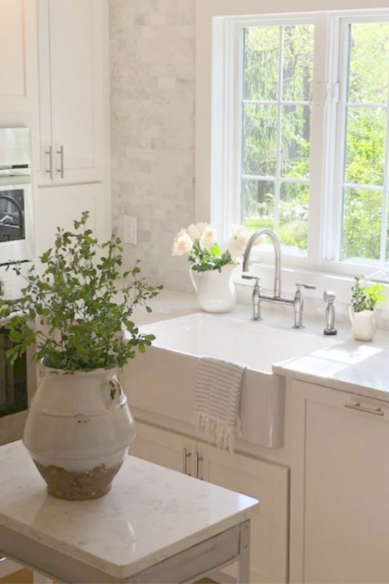 Serene white Shaker kitchen with fireclay farm sink and vintage work cart. Viatera Minuet quartz on counters - hellolovelystudio. Find a Soft, Ethereal European Country Kitchen Mood to Inspire Now!