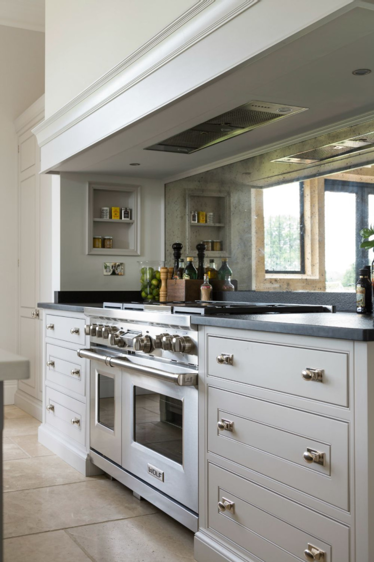 Cornforth White by Farrow & Ball is the paint color on these glorious bespoke kitchen cabinets flanking a range with antiqued mirror backsplash - Humphrey Munson. #paintcolors #cornforthwhtie #farrowandball #kitchencabinets