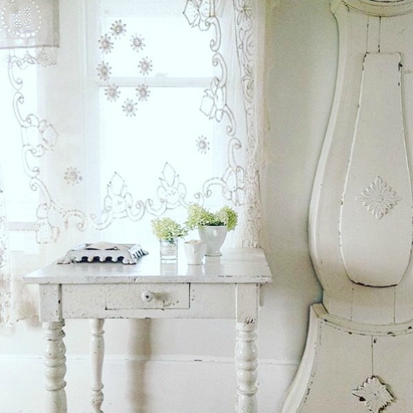 White decor, Swedish Mora clock, lace curtain panel, and vintage painted table add up to French Nordic charm in a white country interior from My Petite Maison.