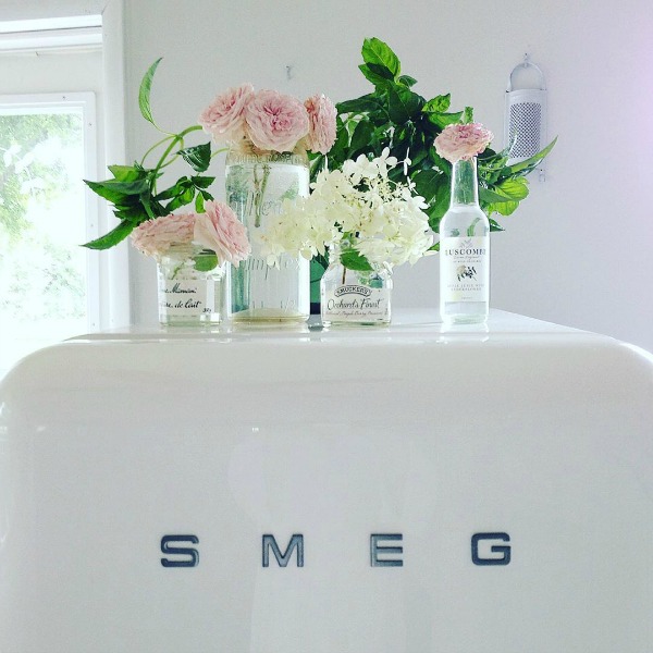 White Smeg refrigerator topped with lovely vintage glass bottles as vases for pink blooms - My Petite Maison.