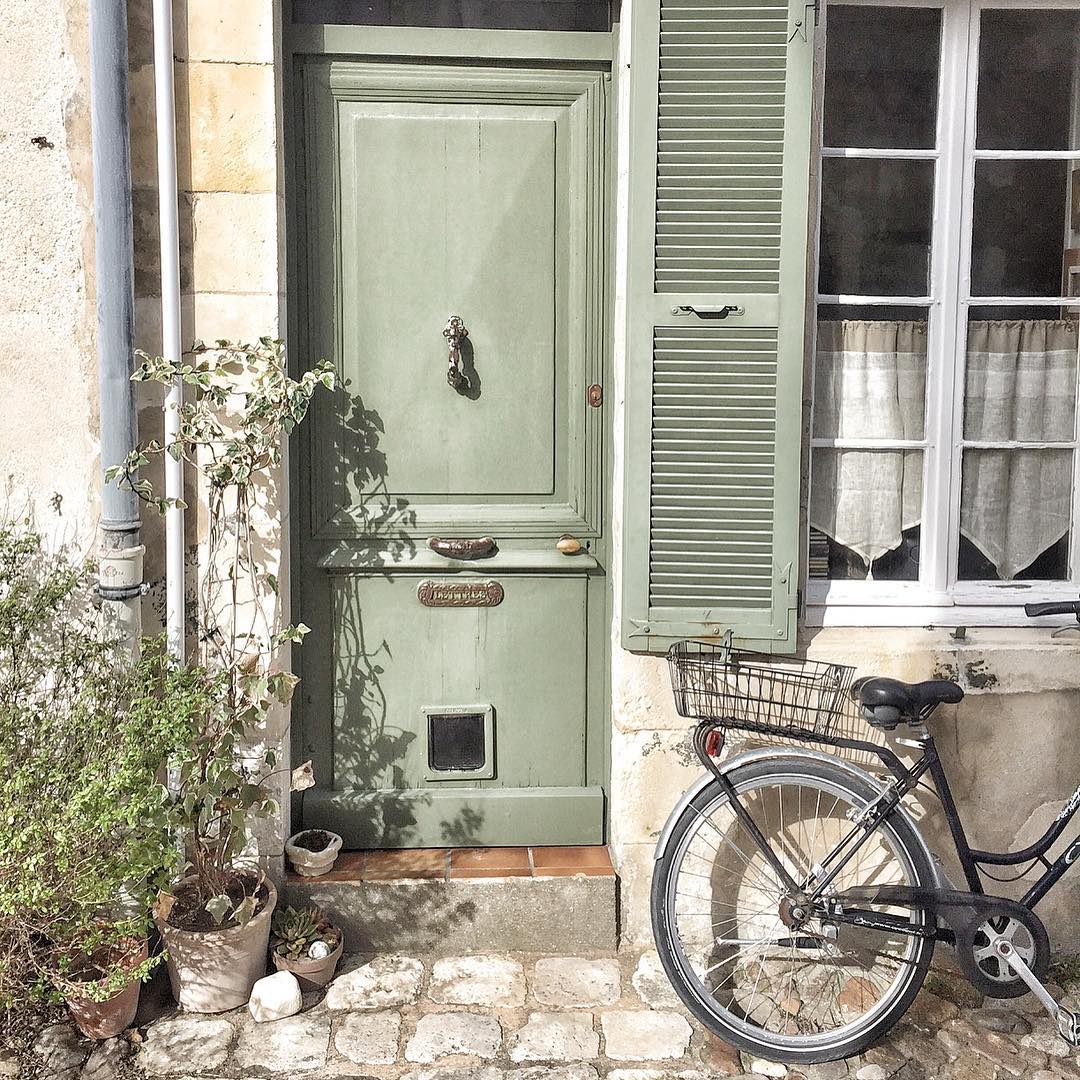 Charming and rustic French farmhouse front door, vintage bicycle, and exterior with Vert Olivier Green Shutters - photo by Vivi et Margot.