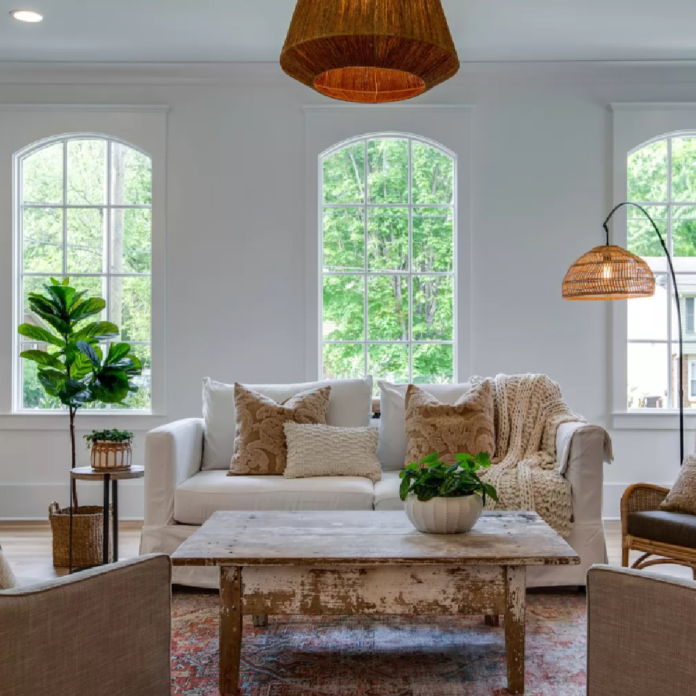 Wicker pendant and white sofa in a netural Southern cottage den with rustic fireplace and raw wood coffee table.