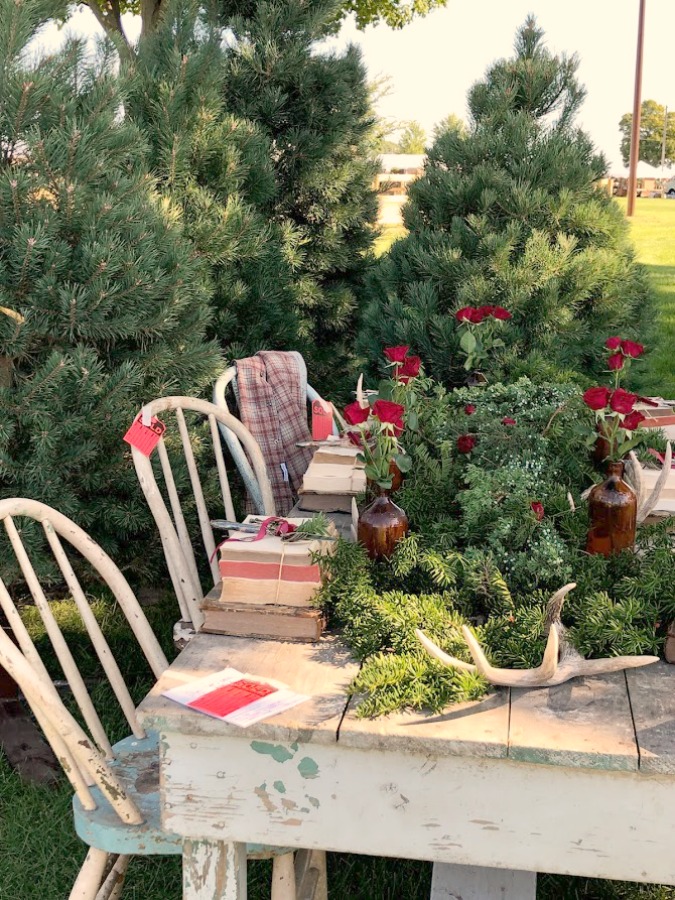 Vintage holiday tablescape outdoors with evergreen trees! Autumn inspiration, Fall farmhouse style decor, vintage wares, and handmade treasures mingle at Main Street Market (Urban Farmgirl) in Belvidere, Illinois - Hello Lovely Studio. #fleamarket #farmhousestyle #vintage #junkin