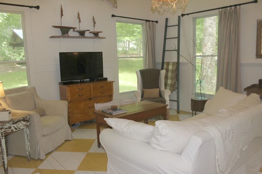 Farmhouse chic living room with vintage treasures, bold yellow painted poplar wood flooring, linen upholstery, and design by City Farmhouse for Storybook Cottage in Leiper's Fork, TN - Hello Lovely Studio. #farmhousestyle #livingroom #cityfarmhouse #storybookcottage