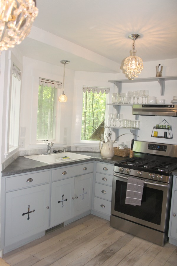 From the blue grey cabinet doors with cross cut out detail to the open shelving, this farmhouse kitchen designed by City Farmhouse for Storybook Cottage in Leiper's Fork, TN, sings with vintage country style! Photo by Hello Lovely Studio. #farmhousekitchen #cityfarmhouse #storybookcottage