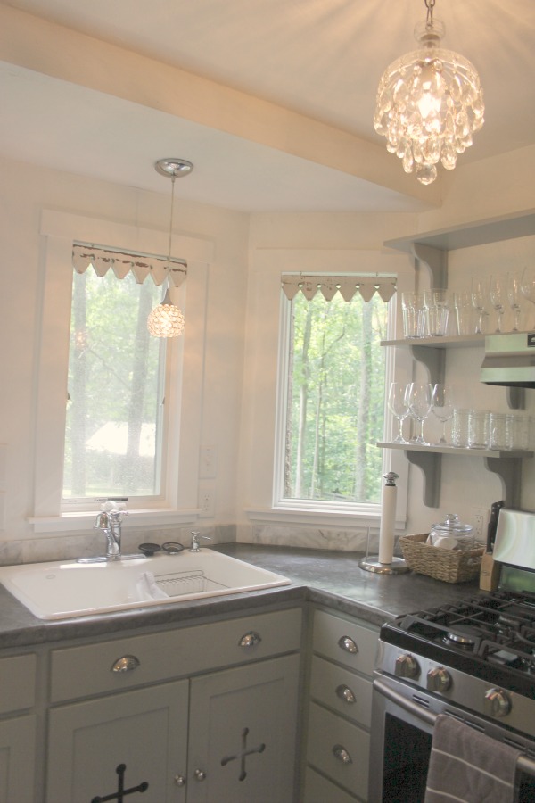 From the blue grey cabinet doors with cross cut out detail to the open shelving, this farmhouse kitchen designed by City Farmhouse for Storybook Cottage in Leiper's Fork, TN, sings with vintage country style! Photo by Hello Lovely Studio. #farmhousekitchen #cityfarmhouse #storybookcottage