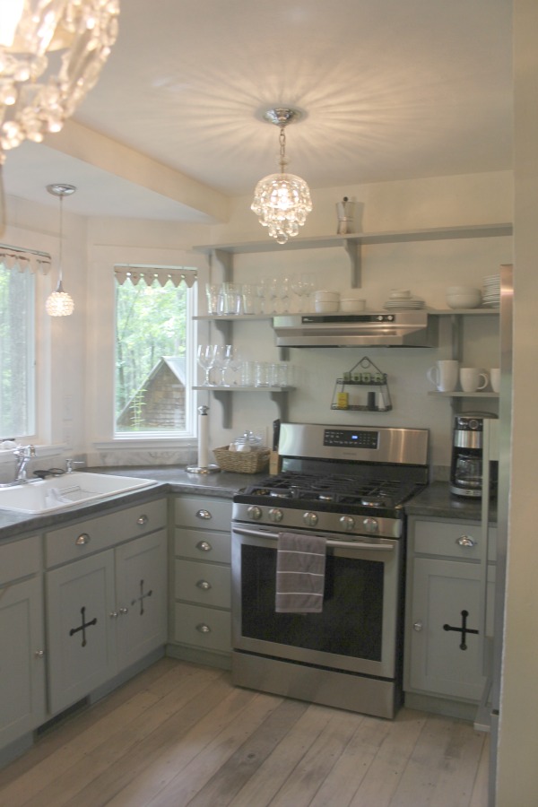 From the blue grey cabinet doors with cross cut out detail to the open shelving, this farmhouse kitchen designed by City Farmhouse for Storybook Cottage in Leiper's Fork, TN, sings with vintage country style! Photo by Hello Lovely Studio. #farmhousekitchen #cityfarmhouse #storybookcottage