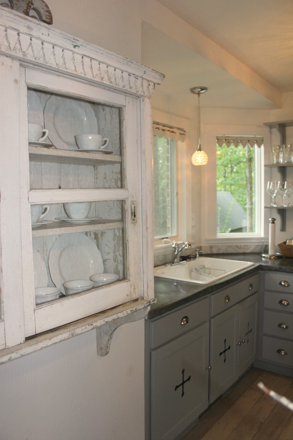 From the blue grey cabinet doors with cross cut out detail to the open shelving, this farmhouse kitchen designed by City Farmhouse for Storybook Cottage in Leiper's Fork, TN, sings with vintage country style! Photo by Hello Lovely Studio. #farmhousekitchen #cityfarmhouse #storybookcottage