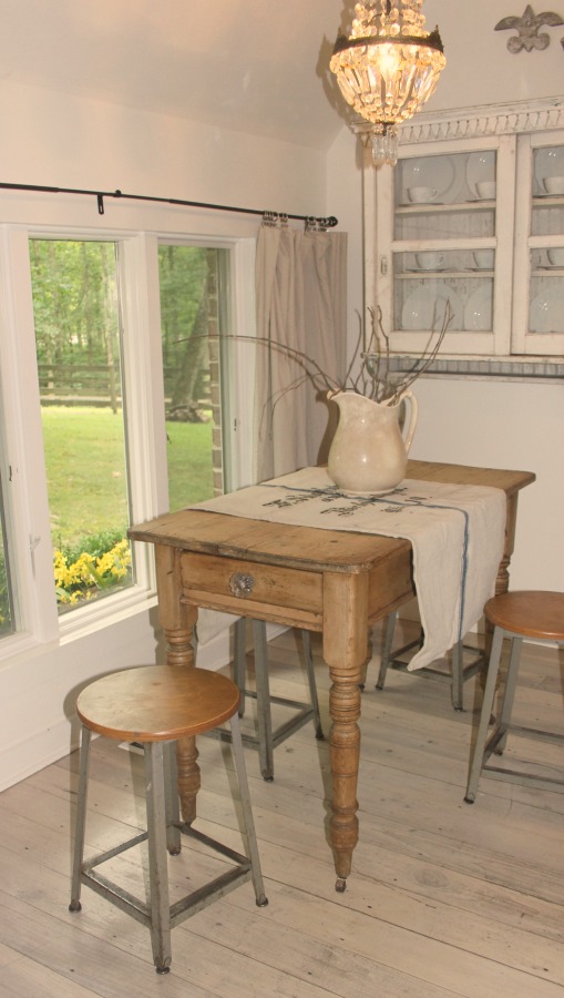 Vintage farmhouse table with turned wood legs and stools is adorned with a vintage German grainsack and ironstone pitcher at Storybook Cottage in Leiper's Fork, TN.