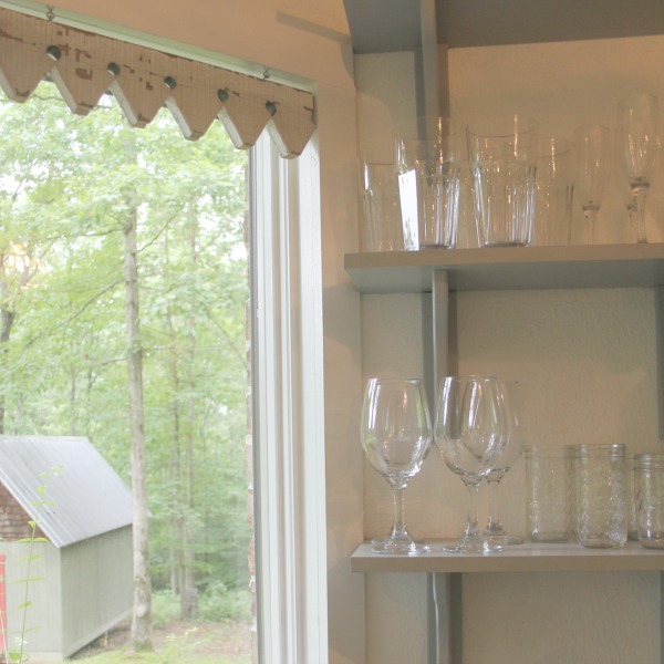 Detail of unique salvaged architectural window treatment. From the blue grey cabinet doors with cross cut out detail to the open shelving, this farmhouse kitchen designed by City Farmhouse for Storybook Cottage in Leiper's Fork, TN, sings with vintage country style! Photo by Hello Lovely Studio. #farmhousekitchen #cityfarmhouse #storybookcottage