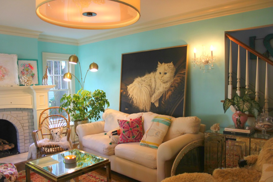 An enormous vintage painting with a fluffy white cat against a bright turquoise painted wall in a colorful boho living room by Jenny Sweeney. #vintagestyle #colorful #interiordesign #boho #whitecat