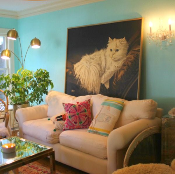 An enormous vintage painting with a fluffy white cat against a bright turquoise painted wall in a colorful boho living room by Jenny Sweeney. Time to Paint Your Walls? Come discover a Refresher to Demystify the Process!