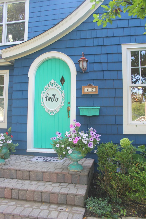 Bold blue painted Tudor cottage with arched door and whimsical front porch decor - Jenny Sweeney! #cottage #exterior #colorful #royalblue #colorfulhome #archdoor