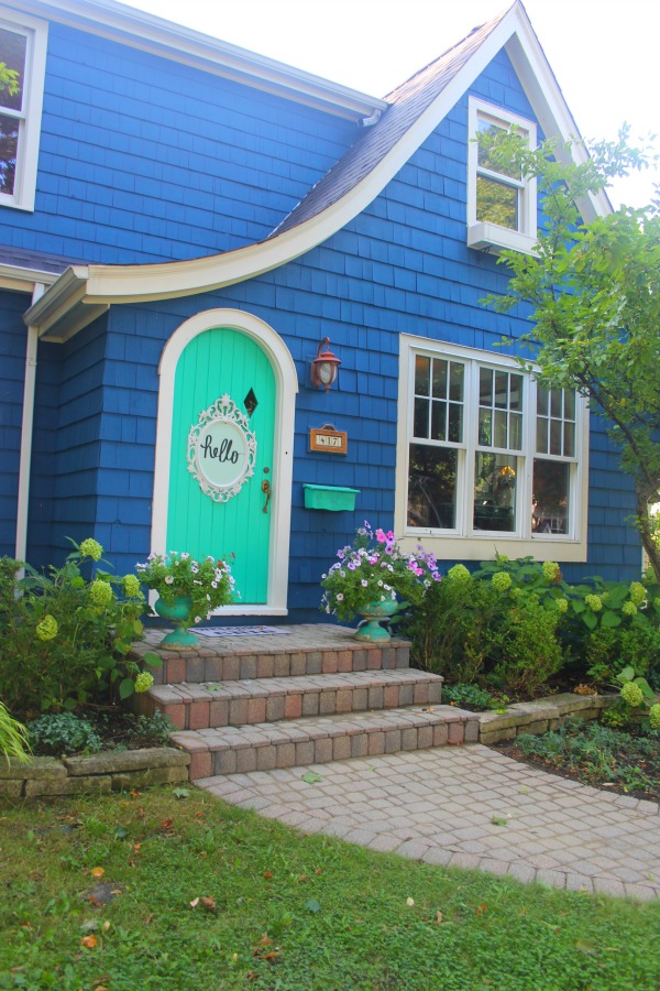 Bold blue painted Tudor cottage with arched door and whimsical front porch decor - Jenny Sweeney! #cottage #exterior #colorful #royalblue #colorfulhome #archdoor