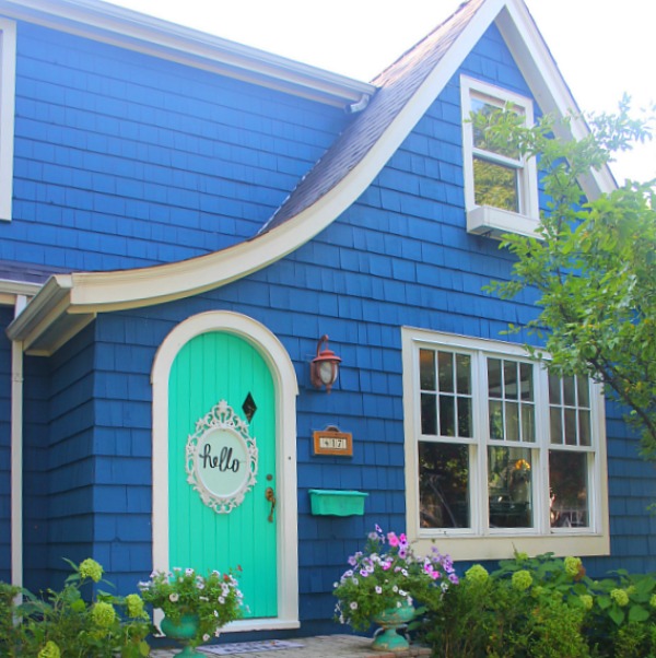 Bold blue painted Tudor cottage with arched door and whimsical front porch decor - Jenny Sweeney! #cottage #exterior #colorful #royalblue #colorfulhome #archdoor