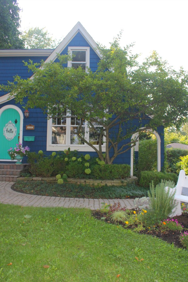 Bold blue painted Tudor cottage with arched door and whimsical front porch decor - Jenny Sweeney! #cottage #exterior #colorful #royalblue #colorfulhome #archdoor