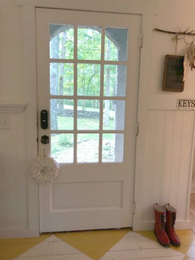 Farmhouse charm and vintage style in a charming entry with white paneling and bold yellow painted poplar floors greeting you at Storybook Cottage in Leiper's Fork near Franklin, TN. The interiors designed by Kim Leggett of City Farmhouse inspire! #farmhousedecor #storybookcottage #entry