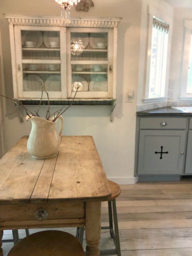 From the blue grey cabinet doors with cross cut out detail to the open shelving, this farmhouse kitchen designed by City Farmhouse for Storybook Cottage in Leiper's Fork, TN, sings with vintage country style! Photo by Hello Lovely Studio. #farmhousekitchen #cityfarmhouse #storybookcottage