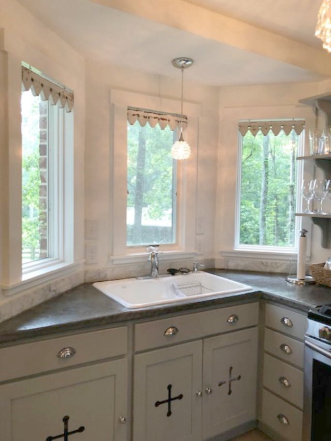 From the blue grey cabinet doors with cross cut out detail to the open shelving, this farmhouse kitchen designed by City Farmhouse for Storybook Cottage in Leiper's Fork, TN, sings with vintage country style! Photo by Hello Lovely Studio. #farmhousekitchen #cityfarmhouse #storybookcottage